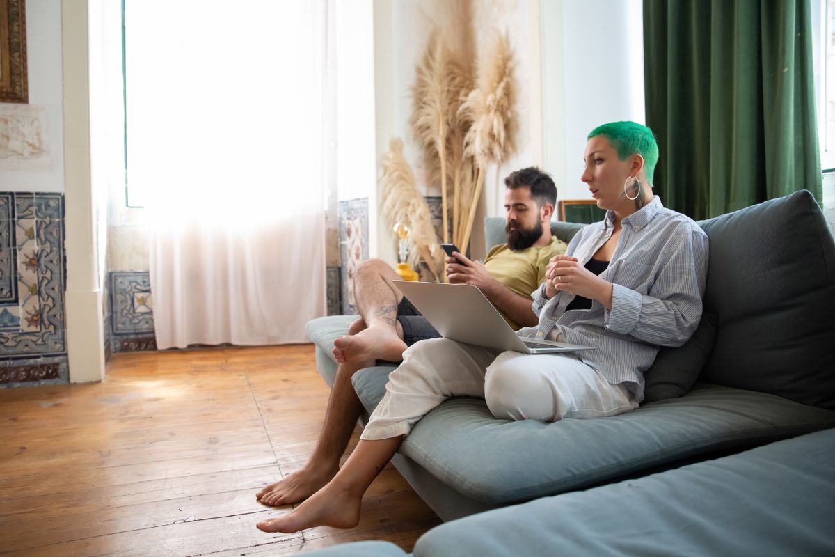 Two people working from a sofa on a laptop